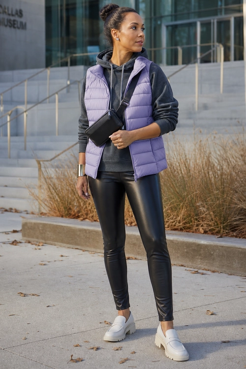 Lavender Puffer Vest with Black Leggings A woman wears a lavender quilted puffer vest over a dark hoodie with black leggings, white loafers, and a black crossbody bag.