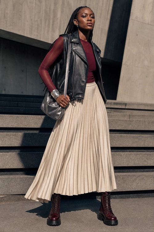 Leather Vest and Pleated Skirt Outfit A burgundy top, black leather vest, cream pleated skirt, burgundy lace-up boots, and metallic shoulder bag styled together on outdoor steps.