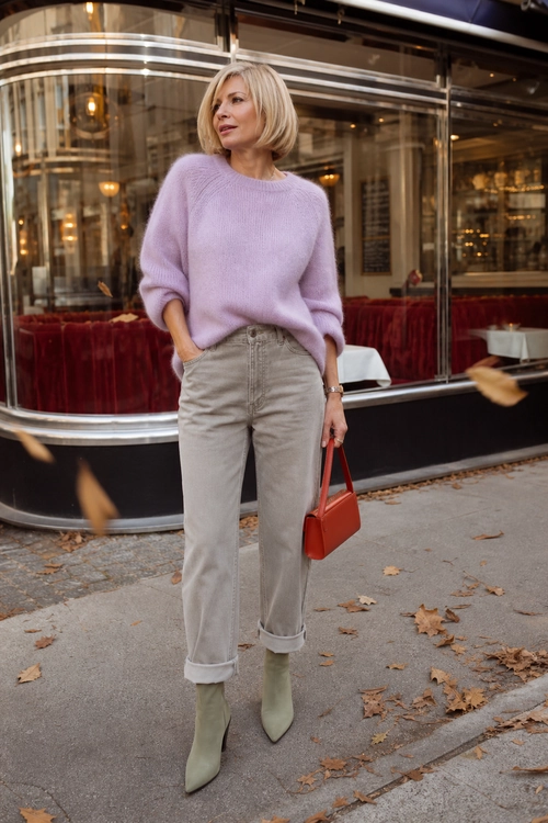 Lilac Sweater and Neutral Jeans A woman wears a soft lilac sweater with light neutral cuffed jeans, pale pointed ankle boots, and a small red handbag.