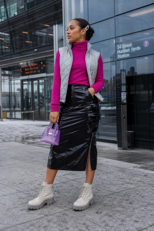Magenta Turtleneck and Quilted Vest Outfit A woman wears a magenta turtleneck, light gray quilted vest, glossy black midi skirt, white lace-up boots, and carries a purple handbag.