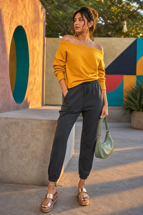 A mustard off-shoulder top paired with charcoal jogger pants, metallic platform sandals, and a sage green shoulder bag.
