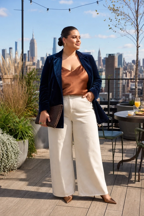 Navy Blazer and Satin Cami A woman wears a navy blazer over a copper satin camisole with white wide-leg trousers, brown pointed heels, hoop earrings, and a dark clutch.