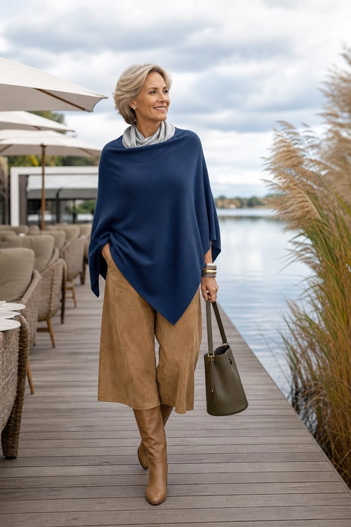 Navy Poncho and Camel Culottes A woman wears a navy poncho with a light gray scarf, camel culottes, tan knee-high boots, and an olive handbag.