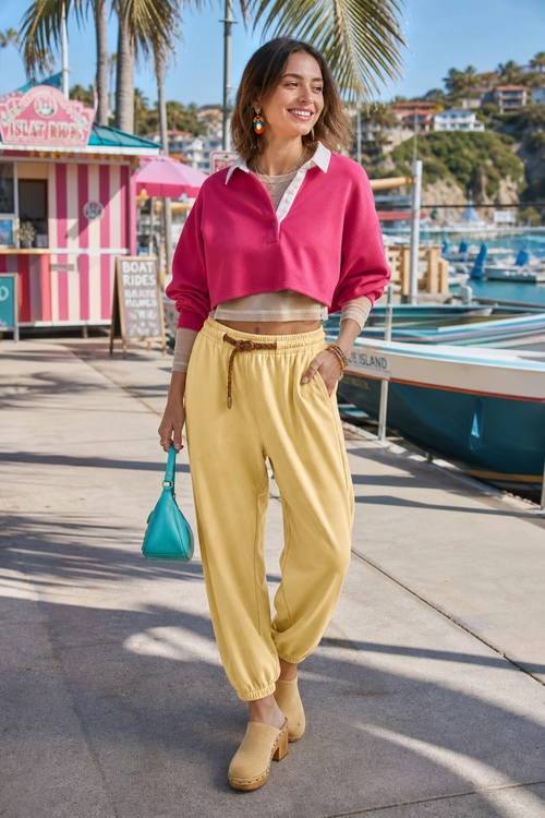 Pink Cropped Top and Yellow Joggers A colorful outfit featuring a pink cropped collared top, yellow jogger pants, tan platform clogs, and a turquoise handbag.