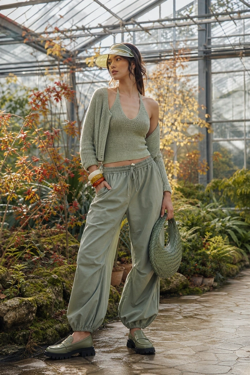 A sage green layered outfit with a knit cardigan, sleeveless top, relaxed jogger pants, visor, woven handbag, and platform loafers.