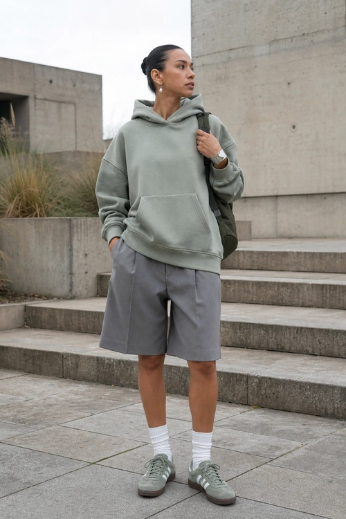 Sage Hoodie and Tailored Shorts Outfit A casual outfit featuring a sage green hoodie, gray knee-length shorts, white socks, gray sneakers, and a dark shoulder bag.