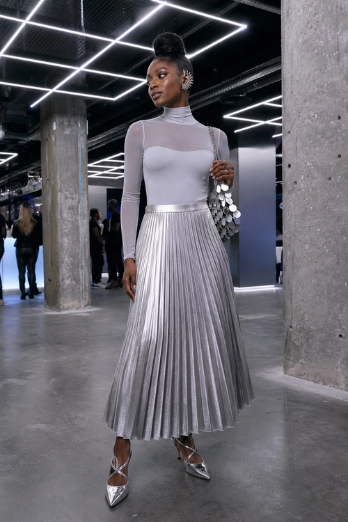 Silver Pleated Skirt Outfit A woman wears a light gray high-neck top with a silver pleated midi skirt, metallic pointed shoes, and a silver disc shoulder bag.