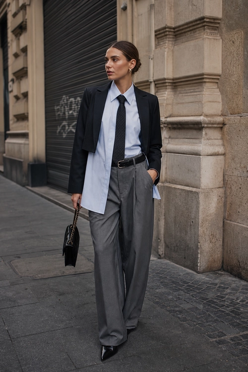 Tailored Shirt and Wide-Leg Trousers A person wears a black blazer, light blue button-down shirt, black tie, gray wide-leg trousers, and pointed black shoes on a city sidewalk.