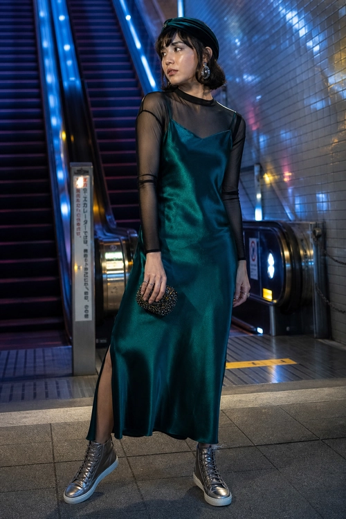 Teal Satin Dress with Sneakers A woman wears a teal satin slip dress layered over a sheer black long-sleeve top with high-top sneakers and a small embellished clutch.