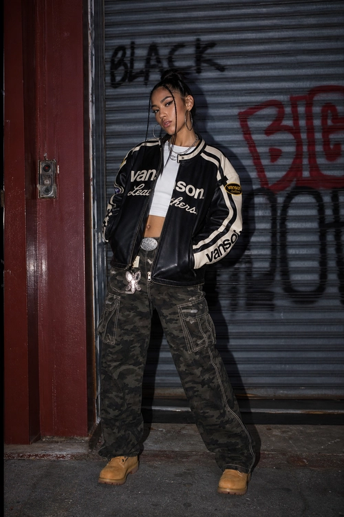 Vans Jacket and Camouflage Cargo Pants Streetwear outfit featuring a black-and-cream Vans jacket, white cropped top, camouflage cargo pants, tan boots, and hoop earrings.