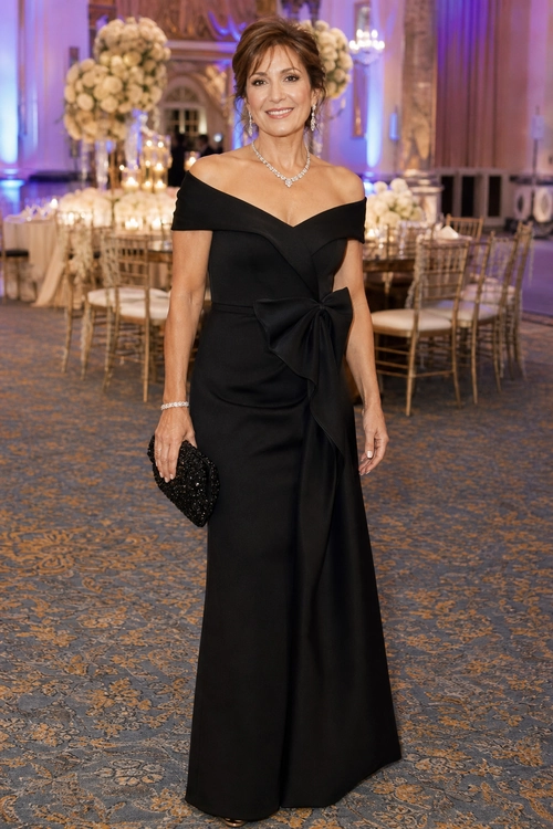 Black Off-Shoulder Gala Gown A woman wears a floor-length black off-shoulder gown with a large waist bow and carries a black beaded clutch at a formal event.