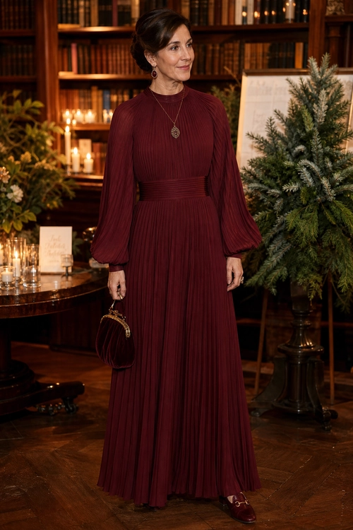 Burgundy Pleated Evening Dress A woman wears a burgundy pleated maxi dress with balloon sleeves, a pendant necklace, matching handbag, and burgundy shoes.