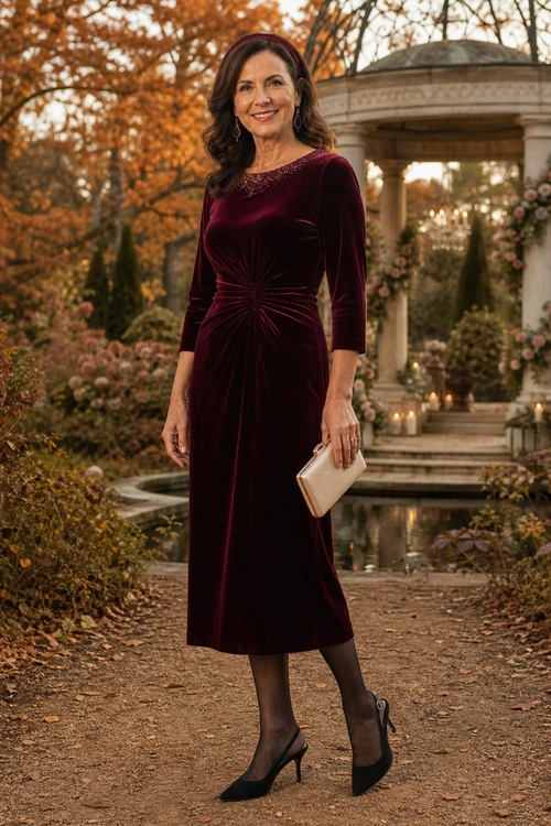Woman wearing a burgundy velvet midi dress with black tights, pointed heels, and a cream clutch in an autumn garden.