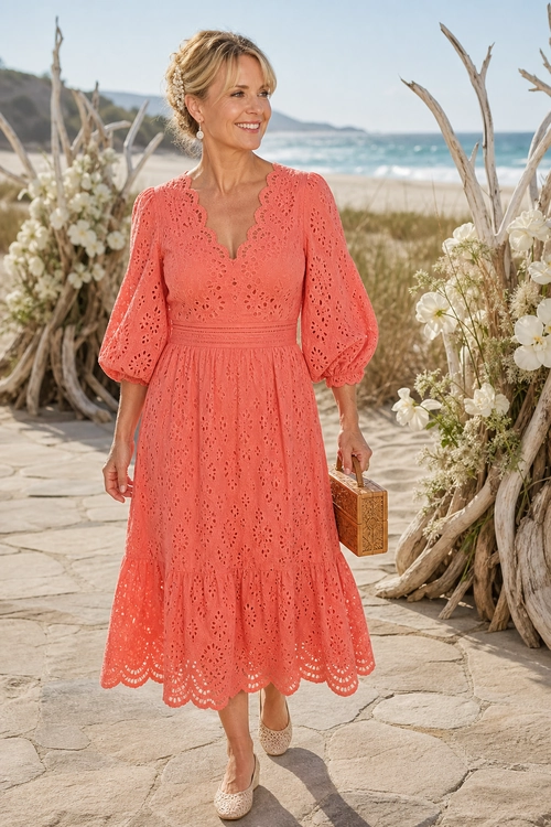 A woman wears a coral eyelet midi dress with puff sleeves, woven beige flats, and a small tan structured handbag.