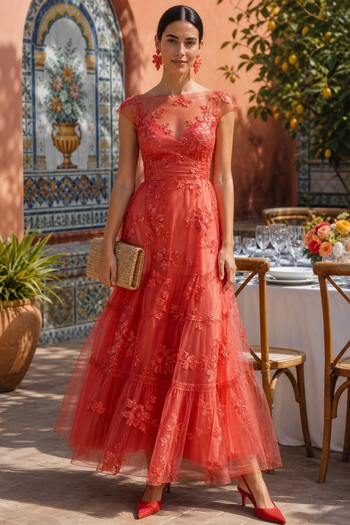 Coral Floral Embroidered Dress A woman wears a coral-red floral embroidered tiered dress with matching pointed heels and carries a woven clutch.