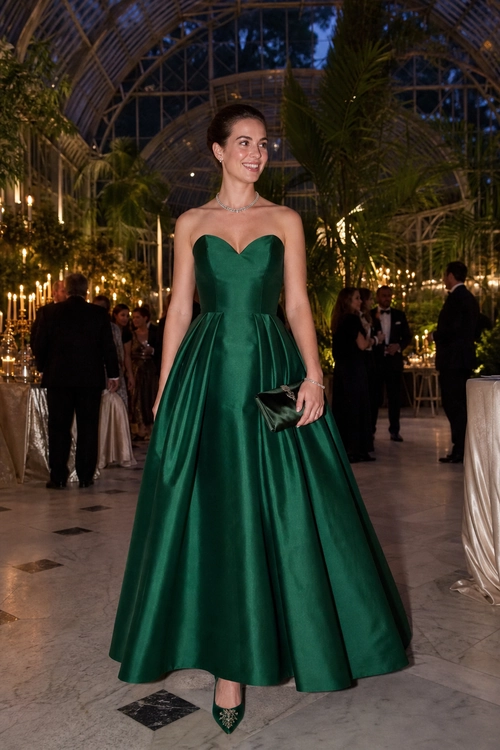 Emerald Green Strapless Evening Gown Woman wearing an emerald green strapless full-skirted evening gown with pointed heels and a small dark clutch at a formal indoor event.