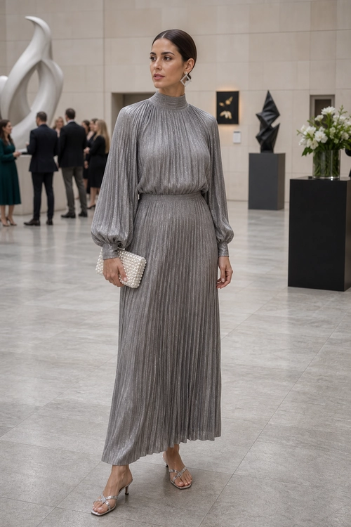 Elegant Gray Pleated Evening Outfit A woman wearing a gray pleated high-neck top and matching long skirt with a beaded clutch and strappy heeled sandals.