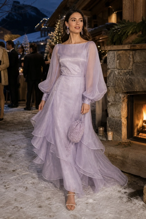 Woman wearing a flowing lavender evening gown with sheer balloon sleeves, tiered ruffles, drop earrings, a beaded clutch, and strappy sandals.