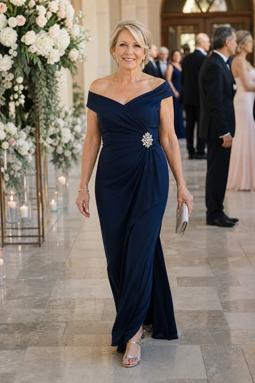 Woman wearing a navy off-the-shoulder draped gown with a jeweled brooch, silver clutch, and metallic sandals at a formal event.