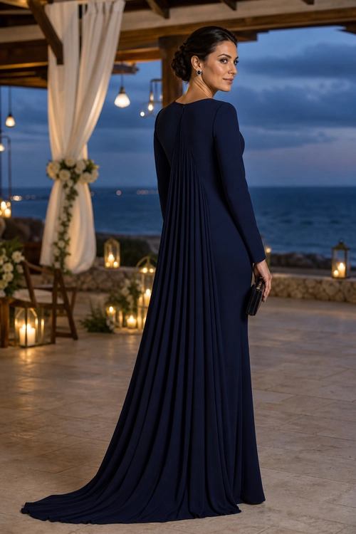 Woman wearing a floor-length navy gown with long sleeves, a pleated back, and a sweeping train while holding a black clutch.