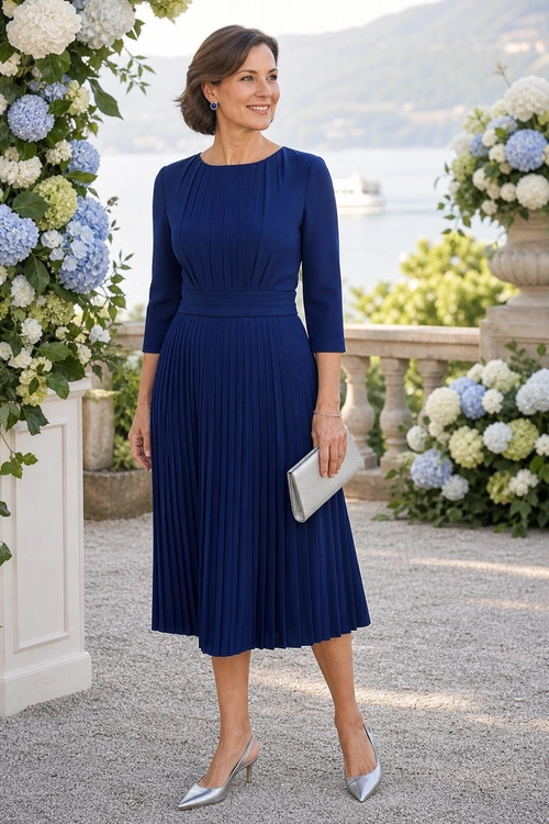 Navy Pleated Midi Dress Outfit Woman wearing a navy pleated midi dress with silver pointed heels and a silver clutch.