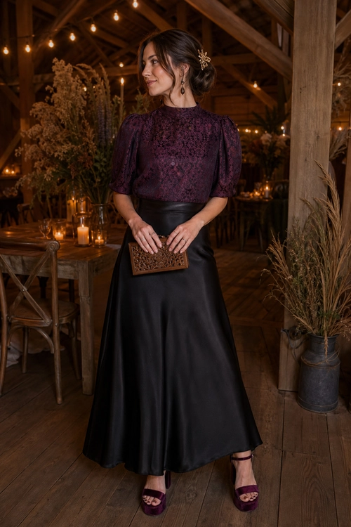 Plum Blouse and Satin Maxi Skirt A woman wears a plum patterned puff-sleeve blouse with a black satin maxi skirt, burgundy heeled sandals, and a decorative clutch.