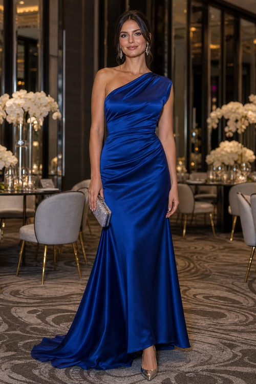 Woman wearing a royal blue one-shoulder satin gown with a silver clutch and metallic pointed heels.