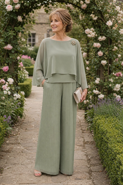 Sage Green Pleated Trouser Outfit A woman wears a sage green layered top with wide-leg pleated trousers, a floral brooch, nude sandals, and a beige clutch in a flower-filled garden.