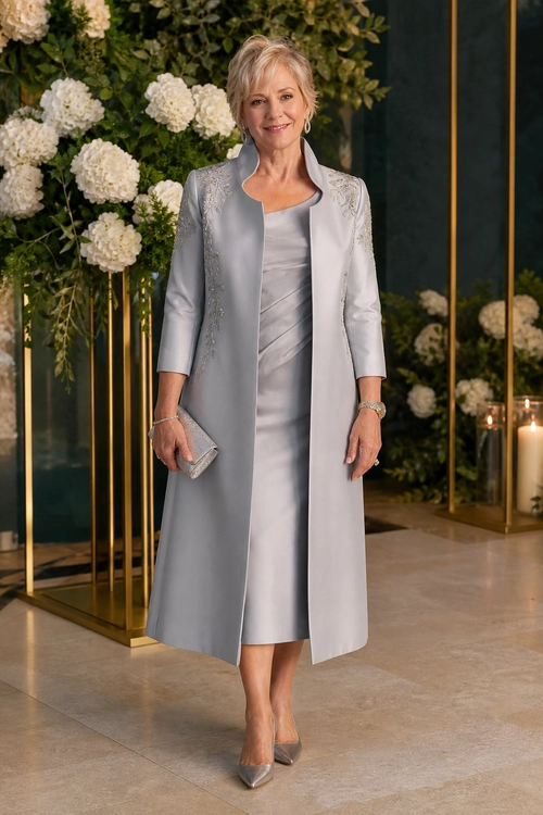 A woman wears a long silver-gray coat over a satin midi dress with pointed metallic pumps and a matching clutch.