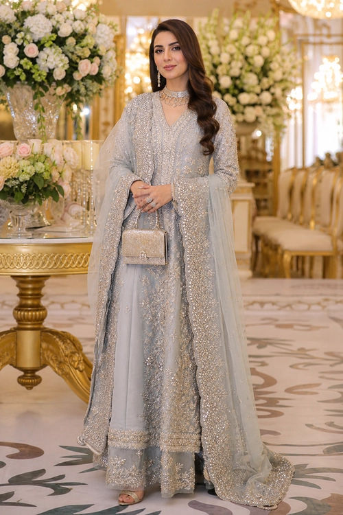 A woman wears a pale silver embellished tunic with wide-leg trousers, a sheer draped dupatta, a matching clutch, and statement jewelry.