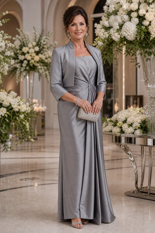 Silver Satin Formal Evening Look A woman wears a silver-gray satin floor-length dress with a cropped matching jacket, metallic clutch, bracelet, and strappy sandals.