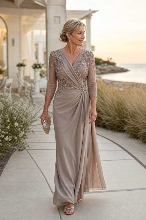 Embellished Taupe Wrap Gown A woman wears a taupe embellished wrap gown with sheer sleeves, strappy sandals, and a small clutch on a seaside walkway.