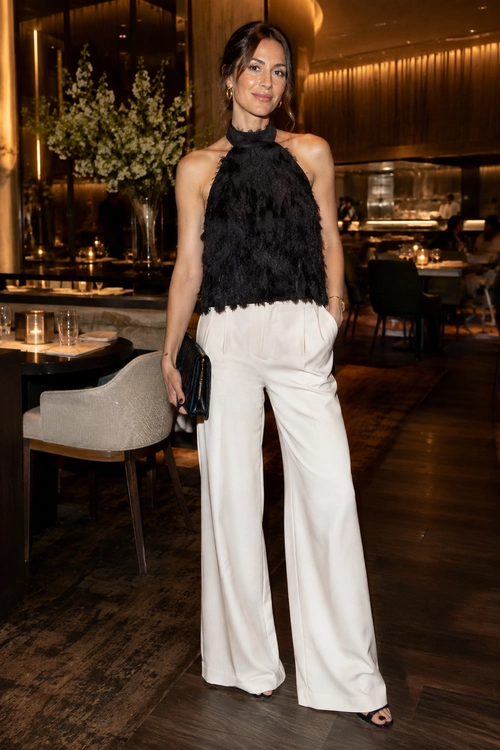 Woman wearing a black textured halter top with white wide-leg trousers, black clutch, and black open-toe sandals.