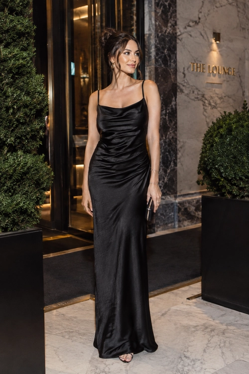 Black Satin Slip Dress Woman wearing a floor-length black satin slip dress with ruched detailing, delicate jewelry, and a small black clutch.
